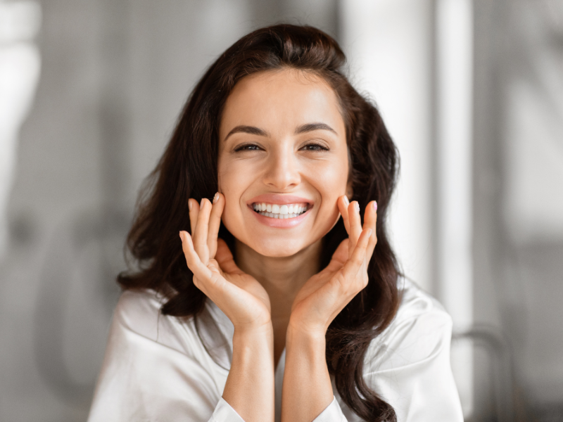 Smiling woman touches her face, showcasing bright and youthful skin