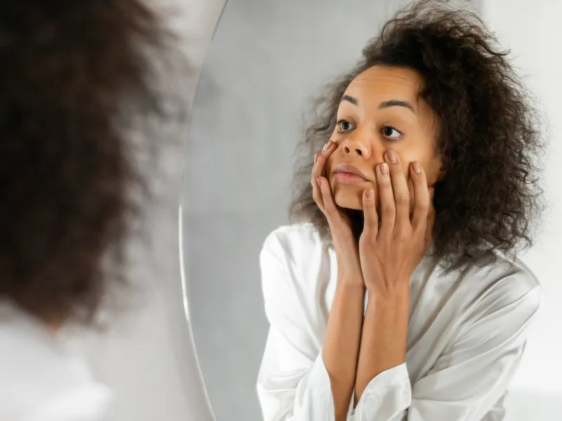 Woman touching her face in the mirror with tired expression