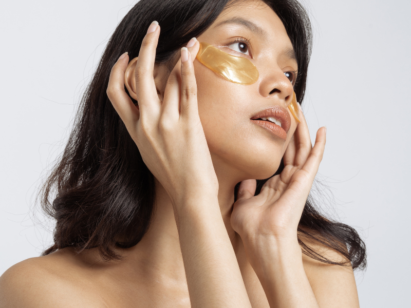 Woman applying golden under-eye patches for hydration and brightness