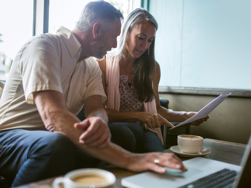 Older couple discussing financial documents while using a laptop in café