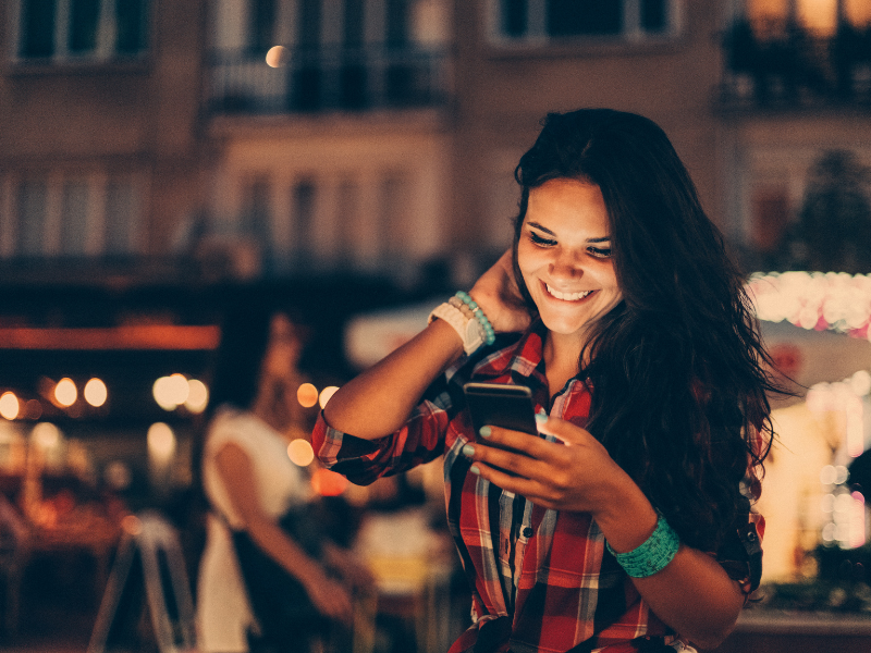Young woman happily checks her phone at a night market
