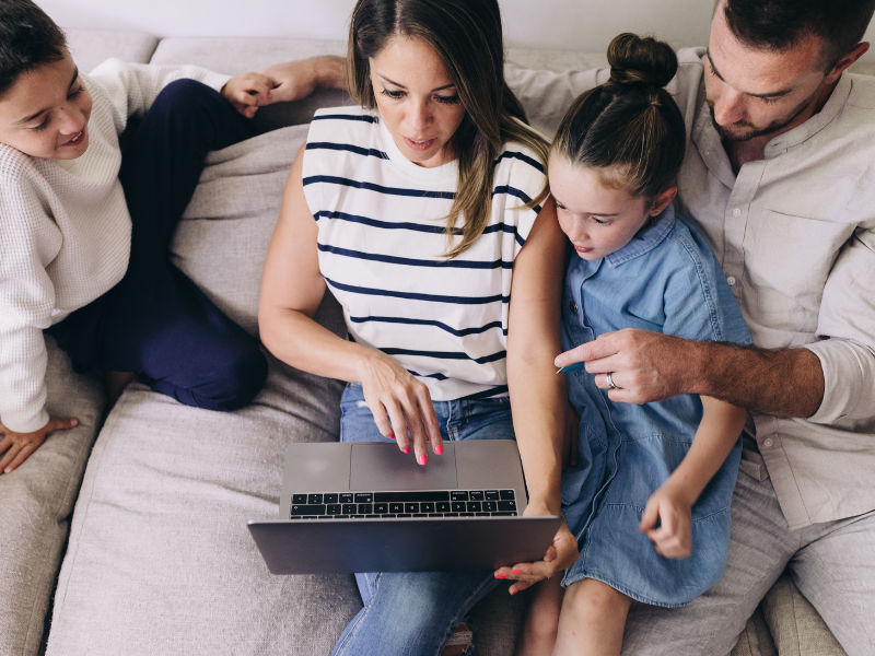 A family sitting on a couch, engaged with a laptop