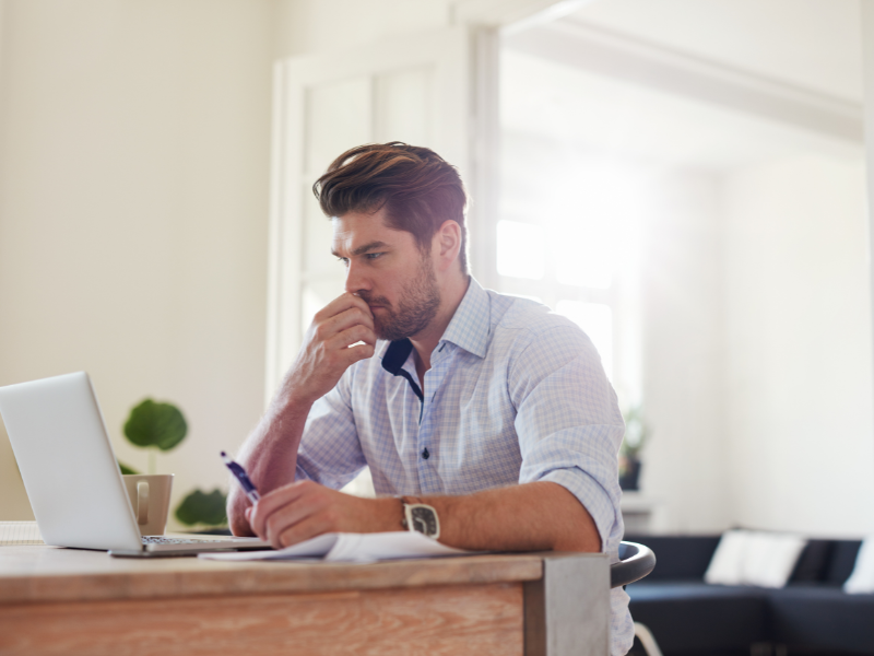Man in blue shirt working on laptop with a thoughtful expression