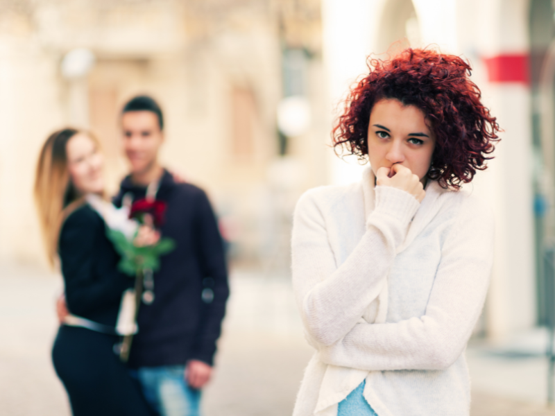 A sad woman watching a happy couple in the background