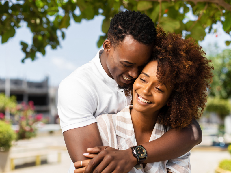Smiling couple embracing each other outdoors under bright sunlight