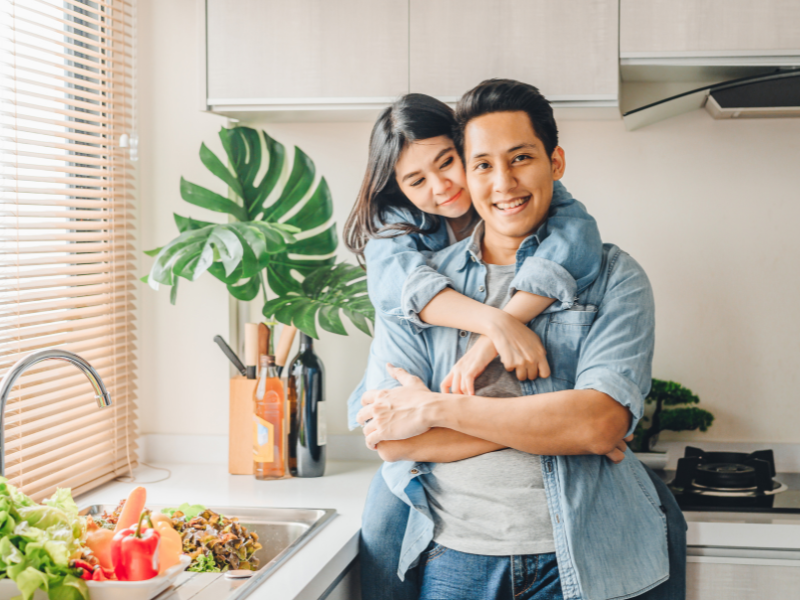 Smiling couple in kitchen hugging while preparing fresh vegetables together