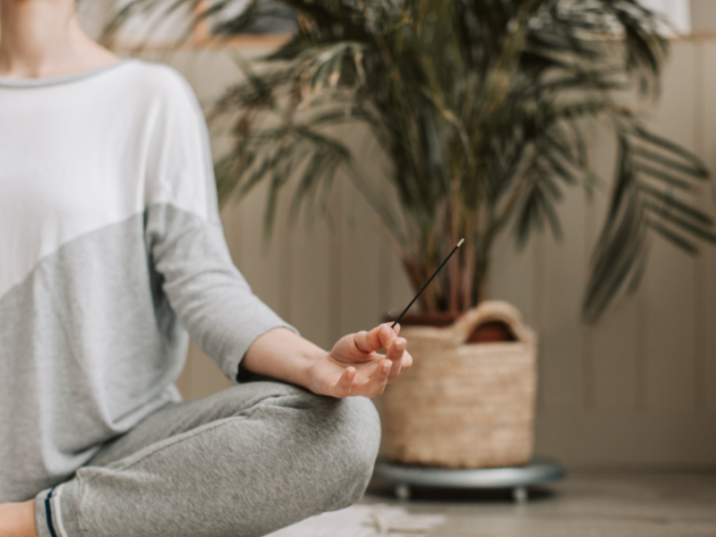 Person meditating with incense stick, sitting cross-legged in peaceful space