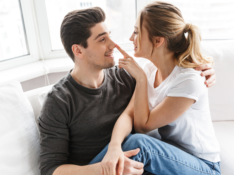 Happy couple sitting on a couch, playfully touching each other’s noses