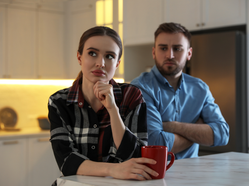 A couple sitting in the kitchen, looking distant and upset