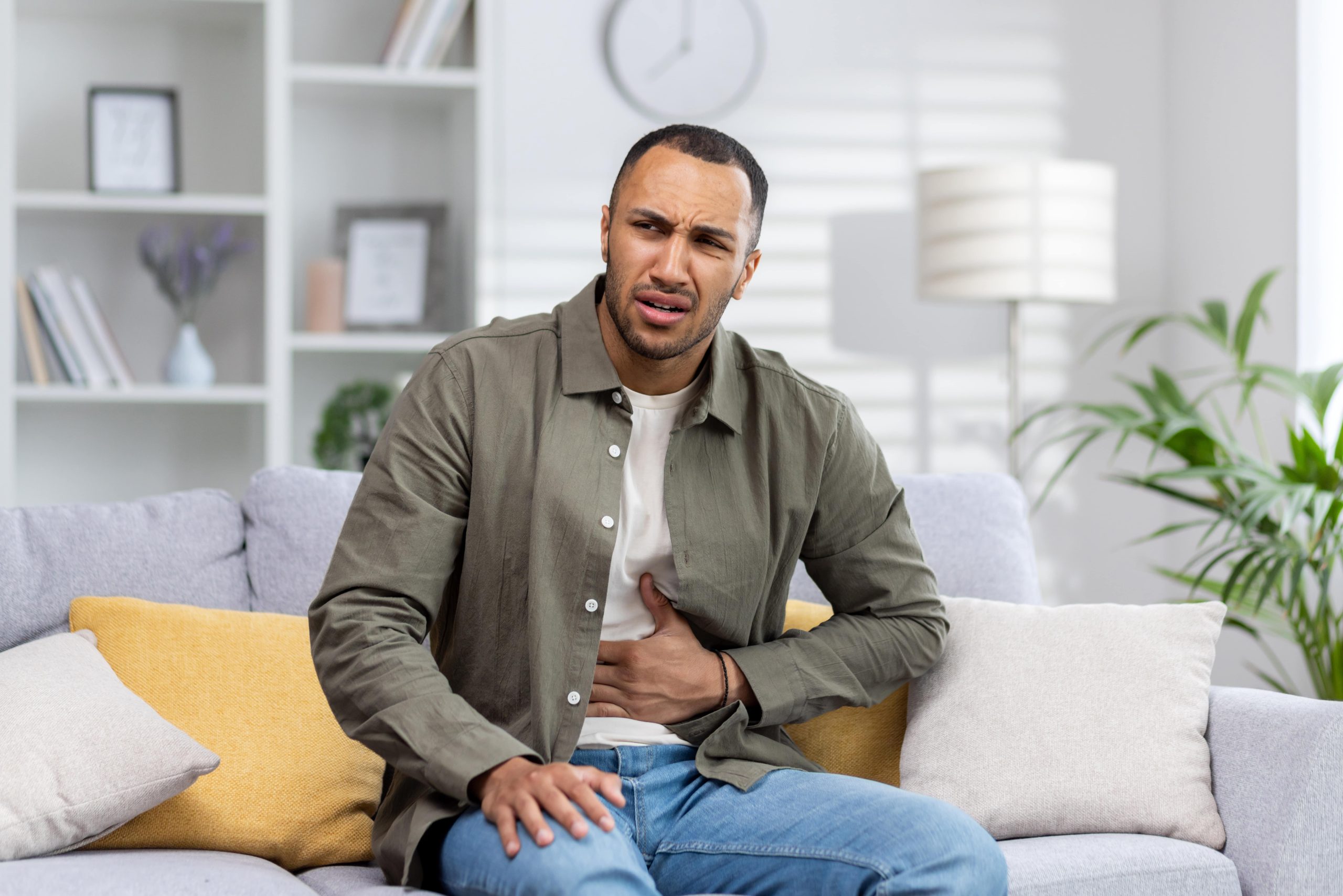 african american sitting on the couch with stomach pain