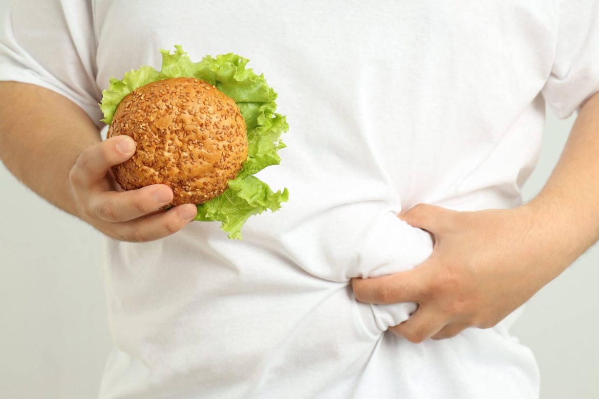 man with stomach pain holding a hamburger