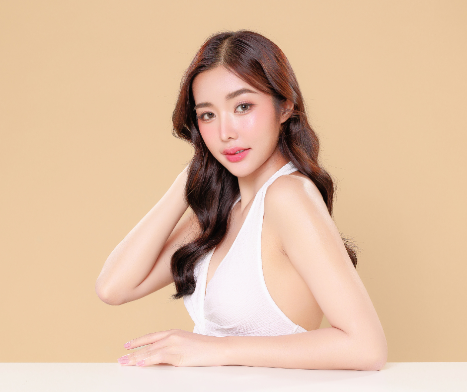 A woman with wavy hair wearing a white sleeveless top, radiating beauty and confidence against a neutral background