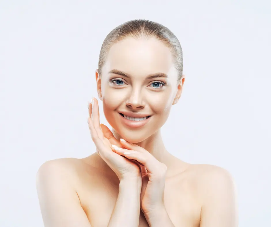 A woman with flawless skin smiling gently while touching her face, highlighting smooth and radiant skin