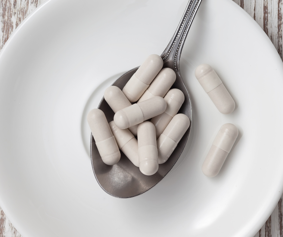 A silver spoon filled with white capsules placed on a white plate, representing high-quality glutathione supplements