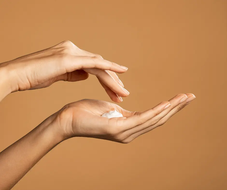 Hands applying moisturizing cream against a neutral background