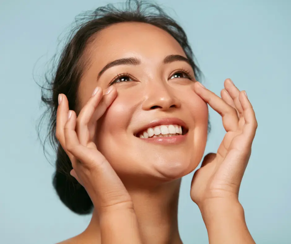 A smiling woman touching her face, showcasing radiant and healthy skin