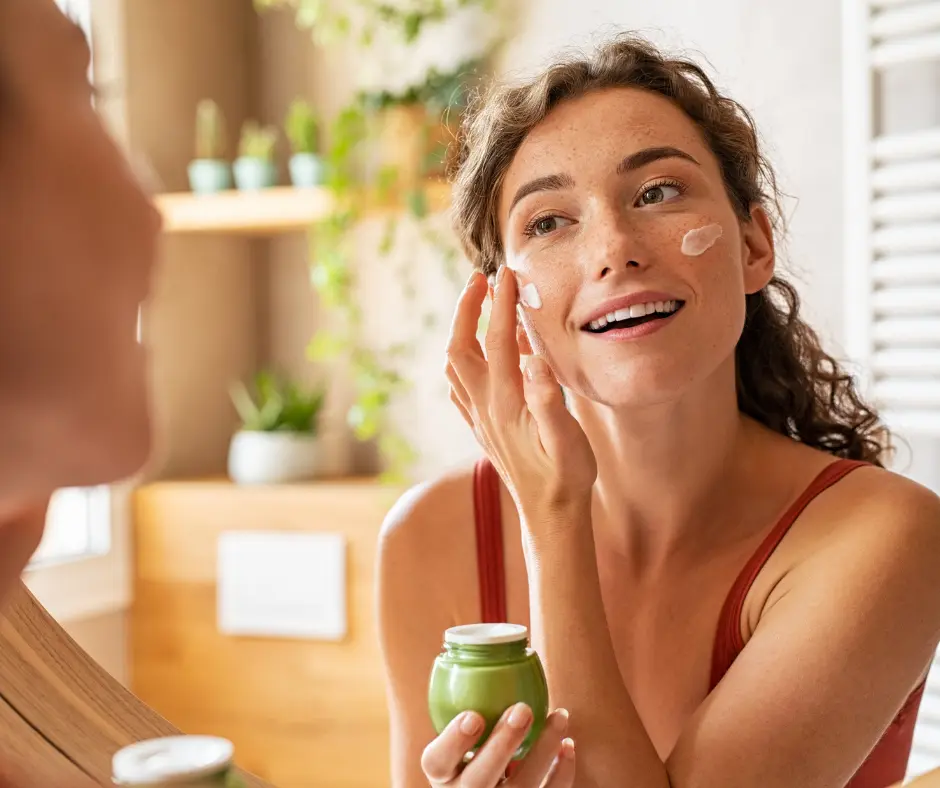 A woman applying cream to her face in a well-lit room