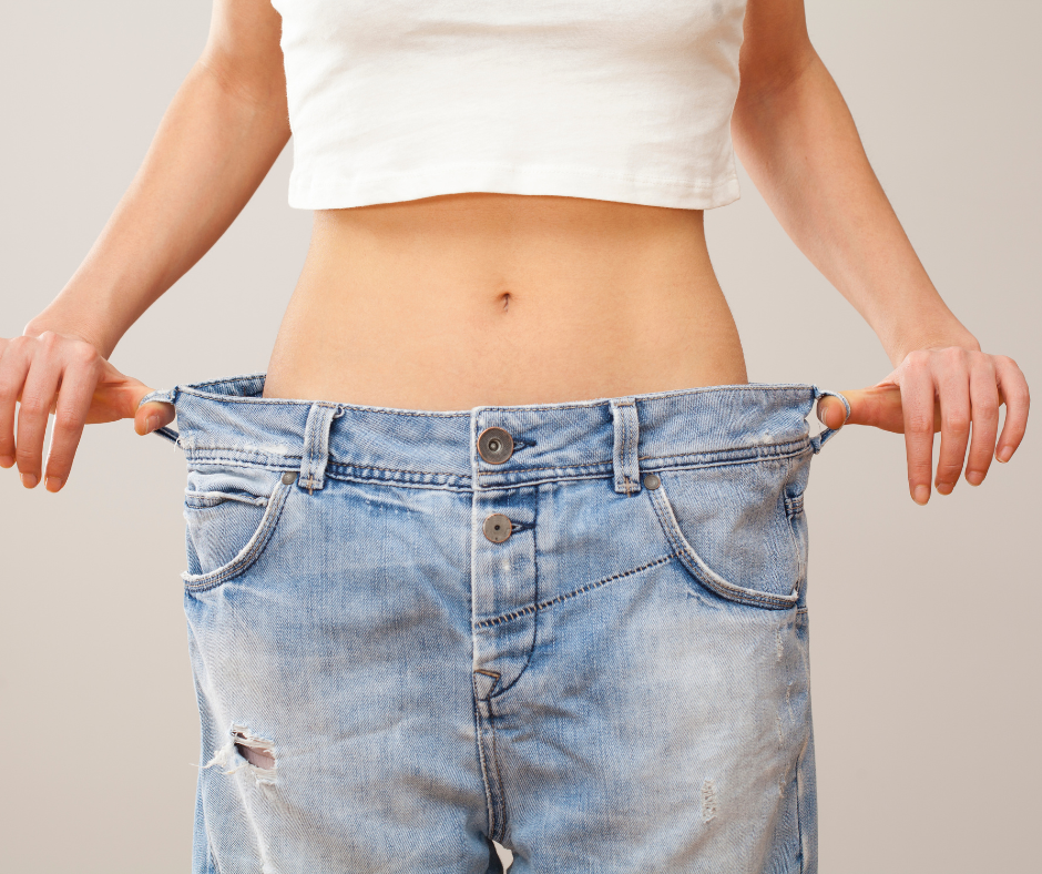 A woman wearing oversized jeans, symbolizing a successful weight loss journey and body transformation