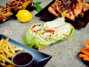 A spread of grilled chicken, crispy fries, and fresh chicken salad wraps wrapped in lettuce, served with barbecue sauce on a rustic table