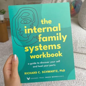 “The Internal Family Systems Workbook being held by a hand in a cozy well light room"