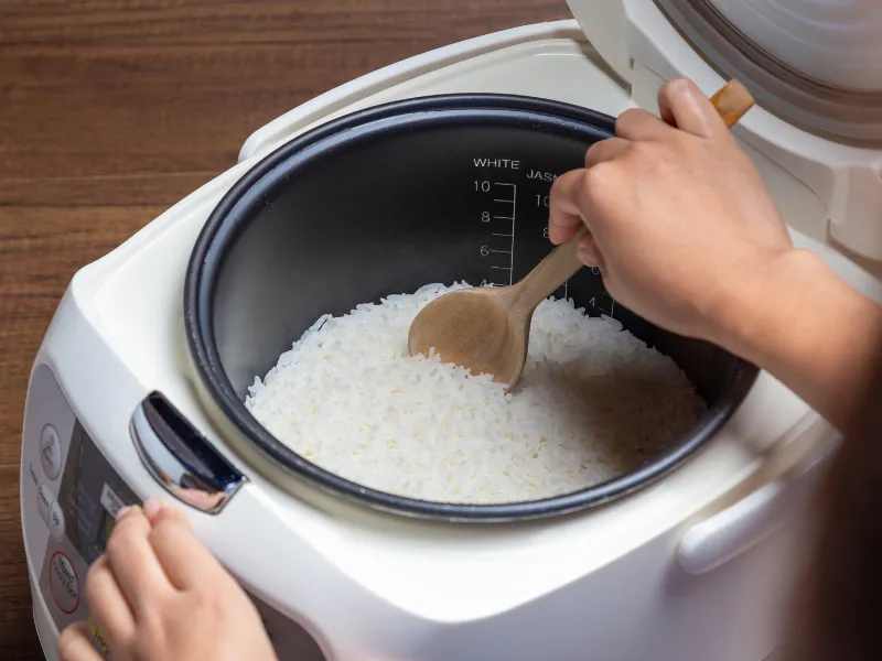 Stirring freshly cooked white rice inside an electric rice cooker