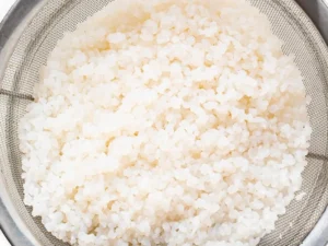 Freshly rinsed shirataki rice in a strainer, ready for cooking