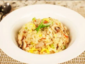 A bowl of fried rice mixed with vegetables, eggs, and mushrooms