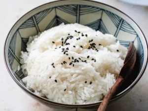 Bowl of steamed rice garnished with black sesame seeds and spoon