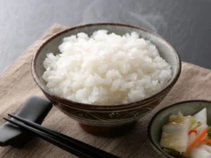 Steamed white rice in a ceramic bowl with chopsticks nearby