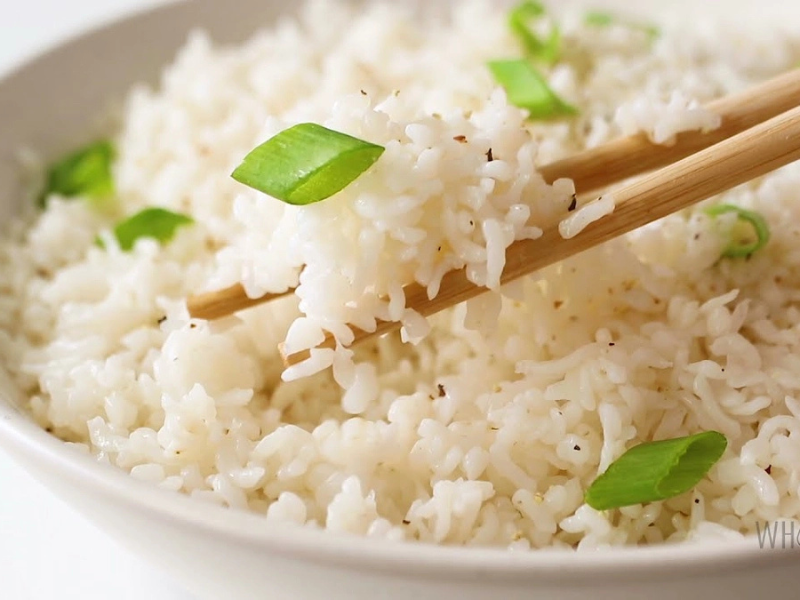 A bowl of steamed white rice with green onion garnish