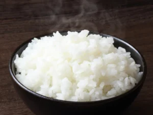 A black bowl filled with hot, steaming white rice