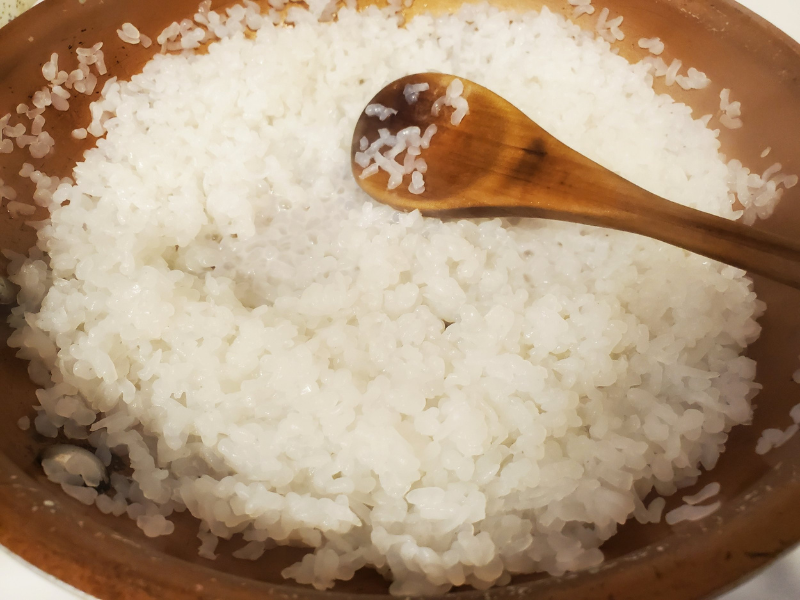 Wooden spoon stirring sticky rice in a copper cooking pot