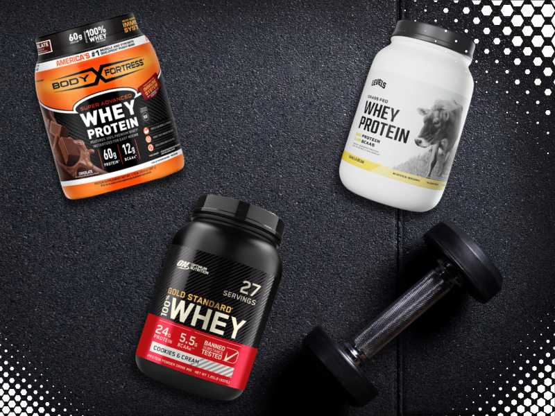 Three whey protein powders and a dumbbell on gym floor