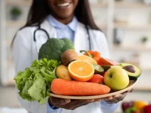 Smiling doctor holding a plate full of fresh fruits and vegetables for healthy skin support.
