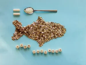 Artistic fish shape made of sequins beside spoon and capsules representing fish collagen supplements