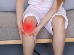 Girl sitting and holding her sore red knee, indicating inflammation or possible joint pain issue